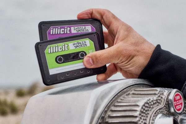 Hand holding an Illicit Smokos pre-roll pack styled like a cassette tape above a vintage car