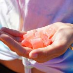 A person holds several pink gummy candies in their open palm, possibly sourced from dispensaries near me. They're wearing a pastel tie-dye shirt and a gold bracelet.