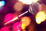 Close-up of a microphone on a stand with colorful, blurred lights in the background, creating a vibrant and energetic atmosphere.