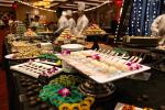 A lavish dessert buffet features an array of colorful sweets and pastries, beautifully arranged on trays and stands, with chefs in white uniforms preparing more treats in the background.
