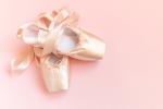 A pair of pale pink ballet pointe shoes with satin ribbons, resting on a light pink background.