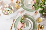 An elegant table setting with pastel-colored eggs in a bowl, plates with pink napkins and tulips, gold cutlery, and flowers in a vase, all arranged for a festive spring or Easter celebration.
